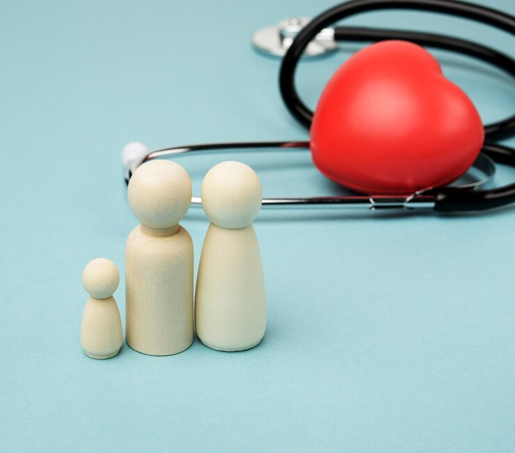 A family of wooden figures of a human family on blue background with a red heart and stethoscope.
