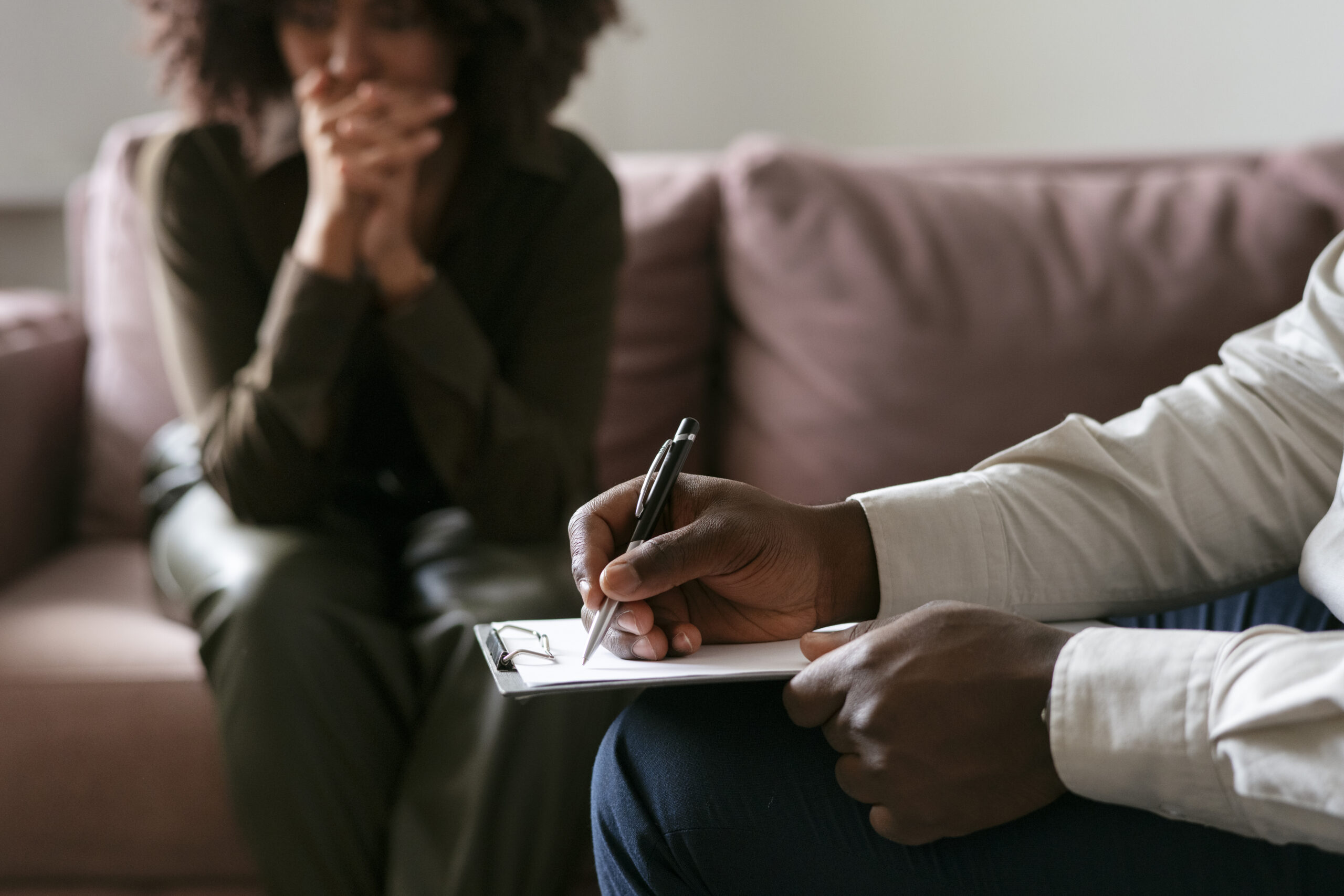 A woman receiving a mental health consultation from a man with a pen and clipboard..